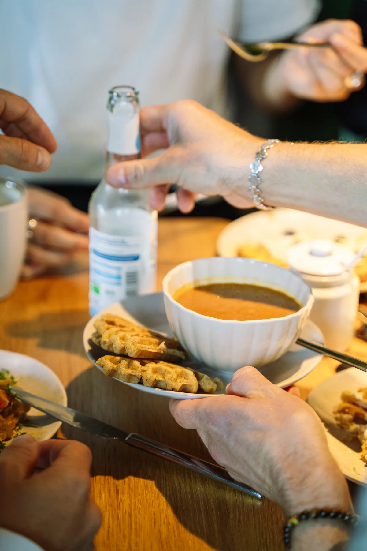 Gäste reichen am Cafétisch eine Schale Suppe mit Waffelstücken weiter